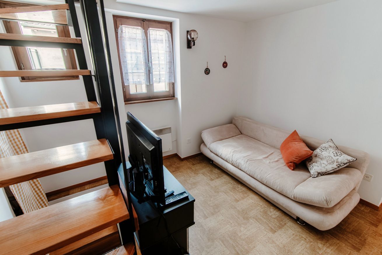 Ein Wohnzimmer mit einer Couch, einem Fernseher und einem Fenster mit Vorhängen.