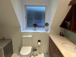 A bathroom with a toilet, sink, vanity, and a window with a view of buildings.