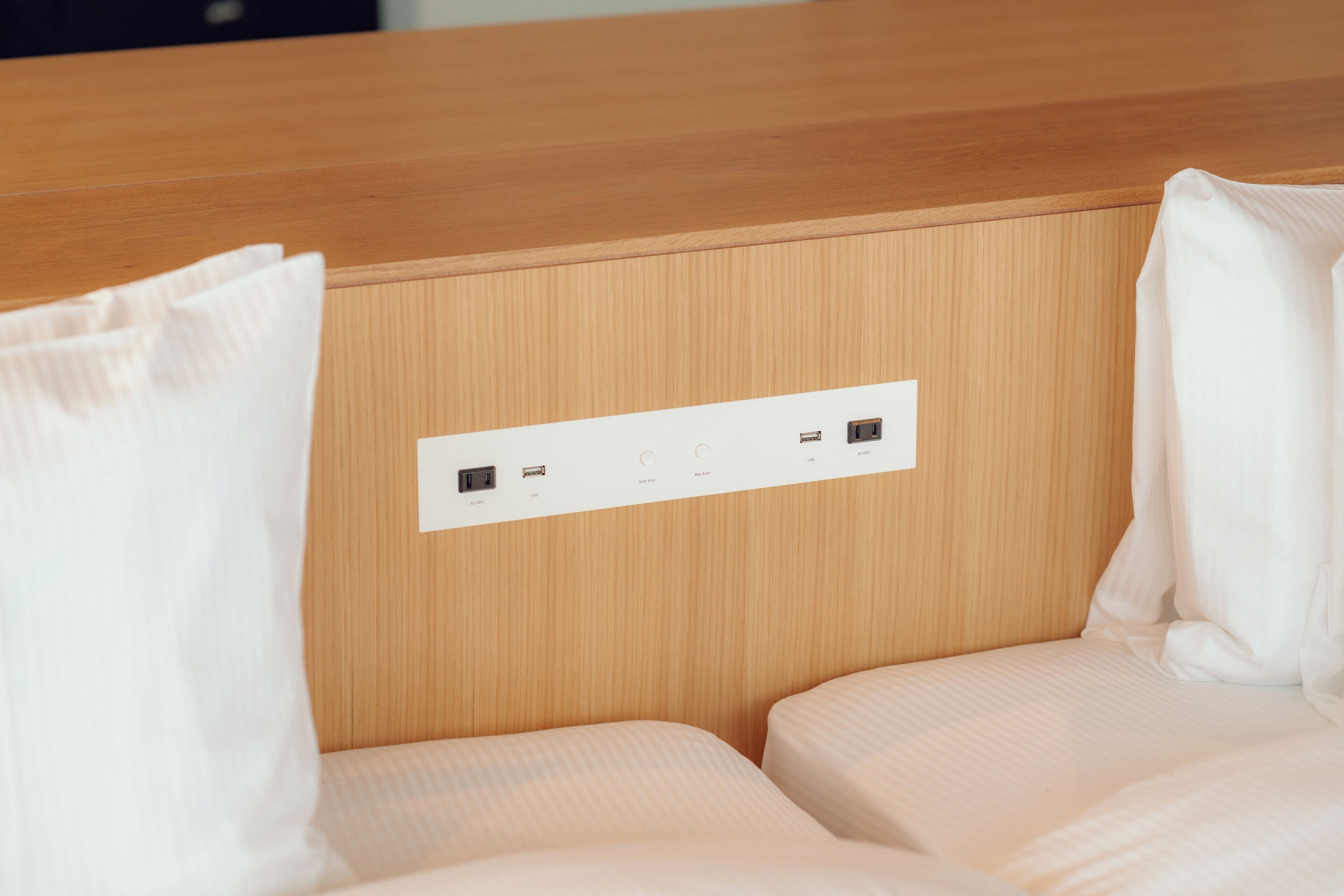 A hotel room with a wooden headboard, two beds, and a control panel with power outlets and USB ports.