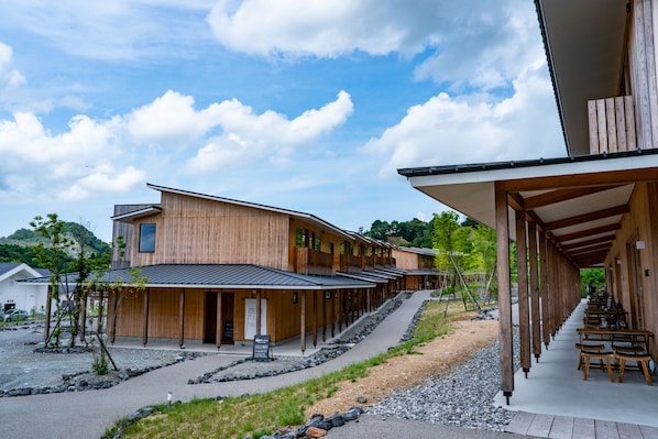 Un edificio moderno de madera con varias habitaciones, un área de estar techada al aire libre y un sendero de grava.