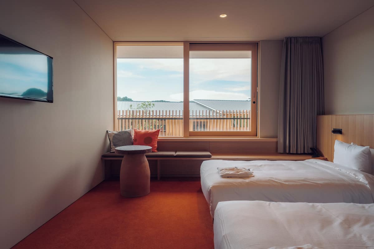 A hotel room with a large window, a bed, a seating area with a round table, and a TV mounted on the wall.
