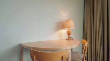 Et lille rundt bord med en lampe, en stol og et gardin i baggrunden.
