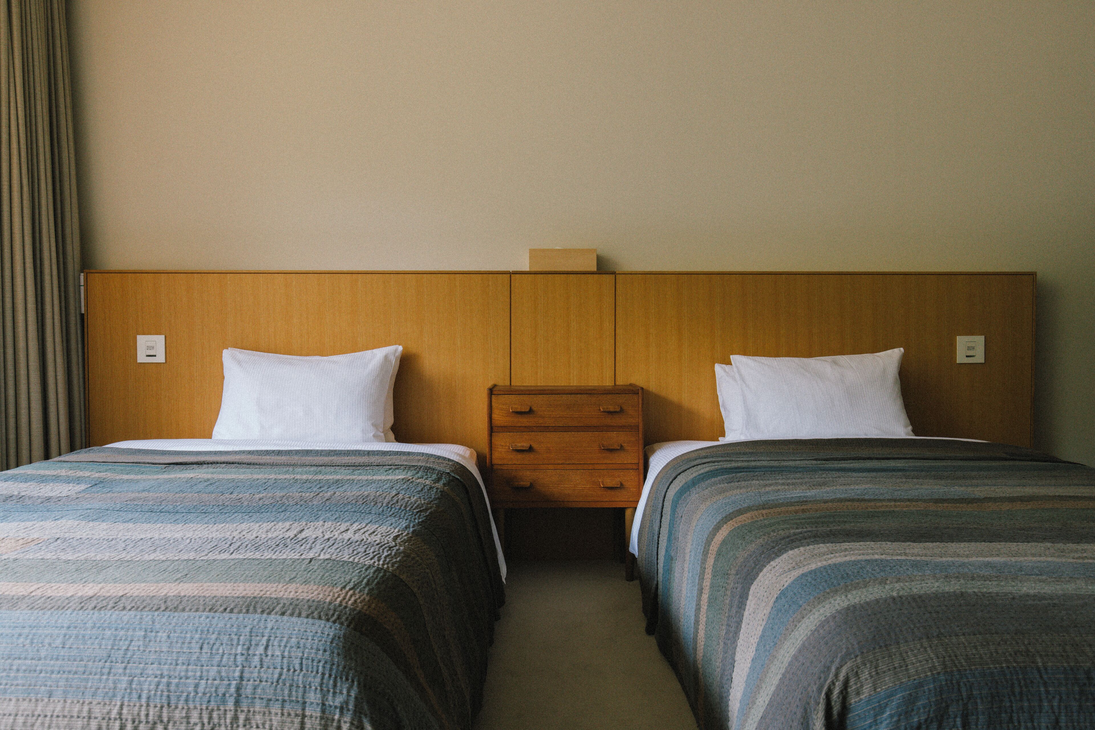 Ein Hotelzimmer mit zwei Betten, einem Holz-Kopfteil und einem Nachttisch mit Schubladen.