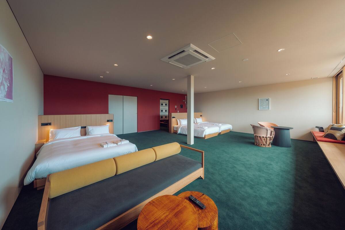 A hotel room with a large bed, a sofa, a small table, and a chair. There are two beds in the room.