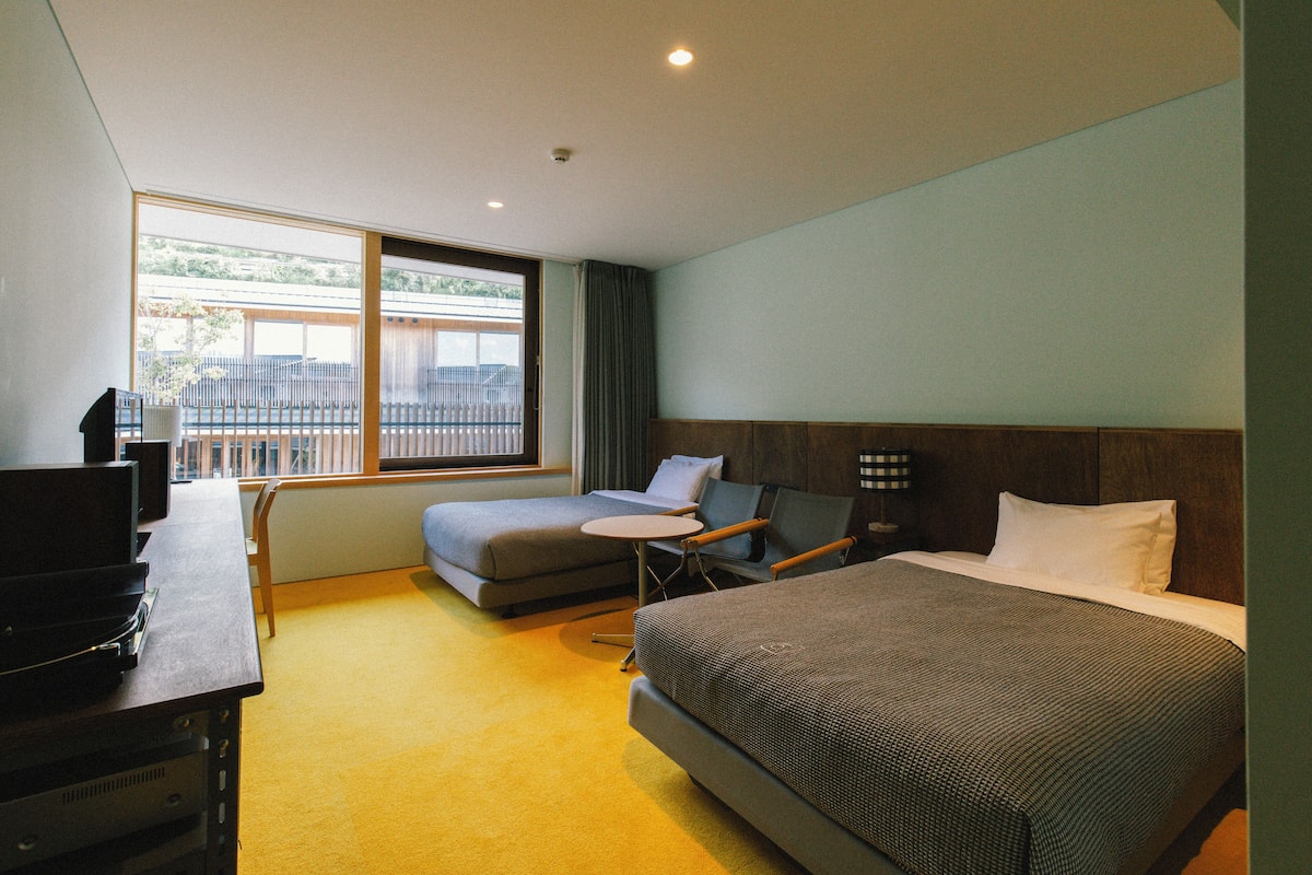 A hotel room with a bed, a desk with a computer, a chair, and a small table.