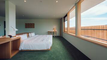 A hotel room with a large bed, a wooden desk, a small table, and a window with a view of a wooden fence.