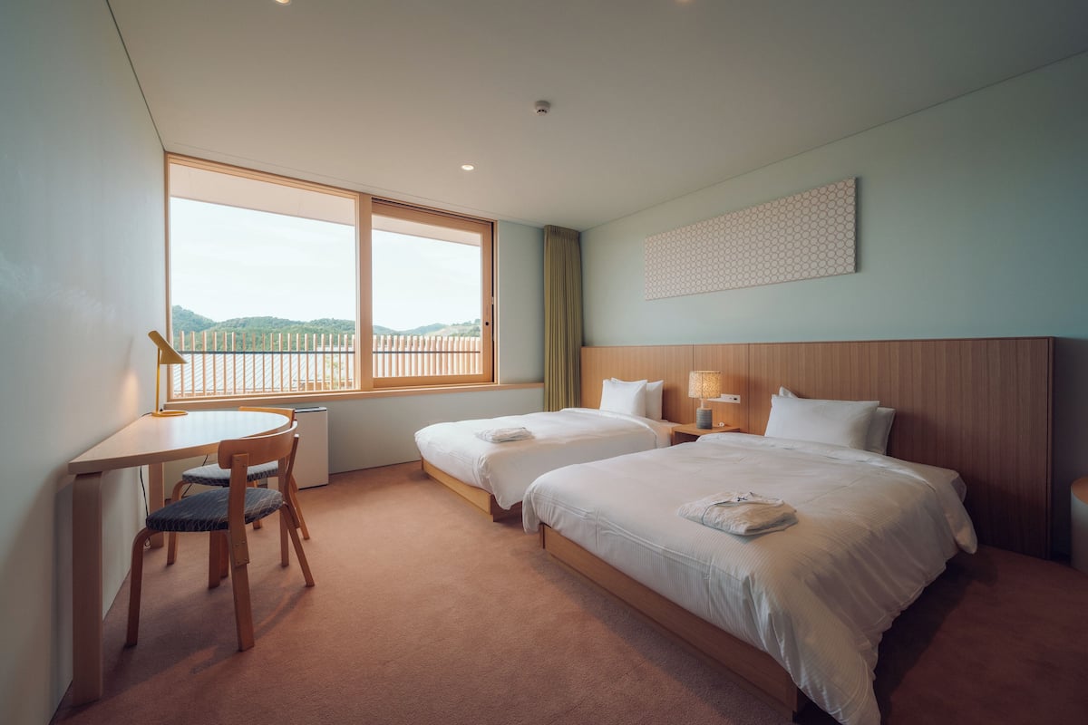 A hotel room with two beds, a desk, and a chair.