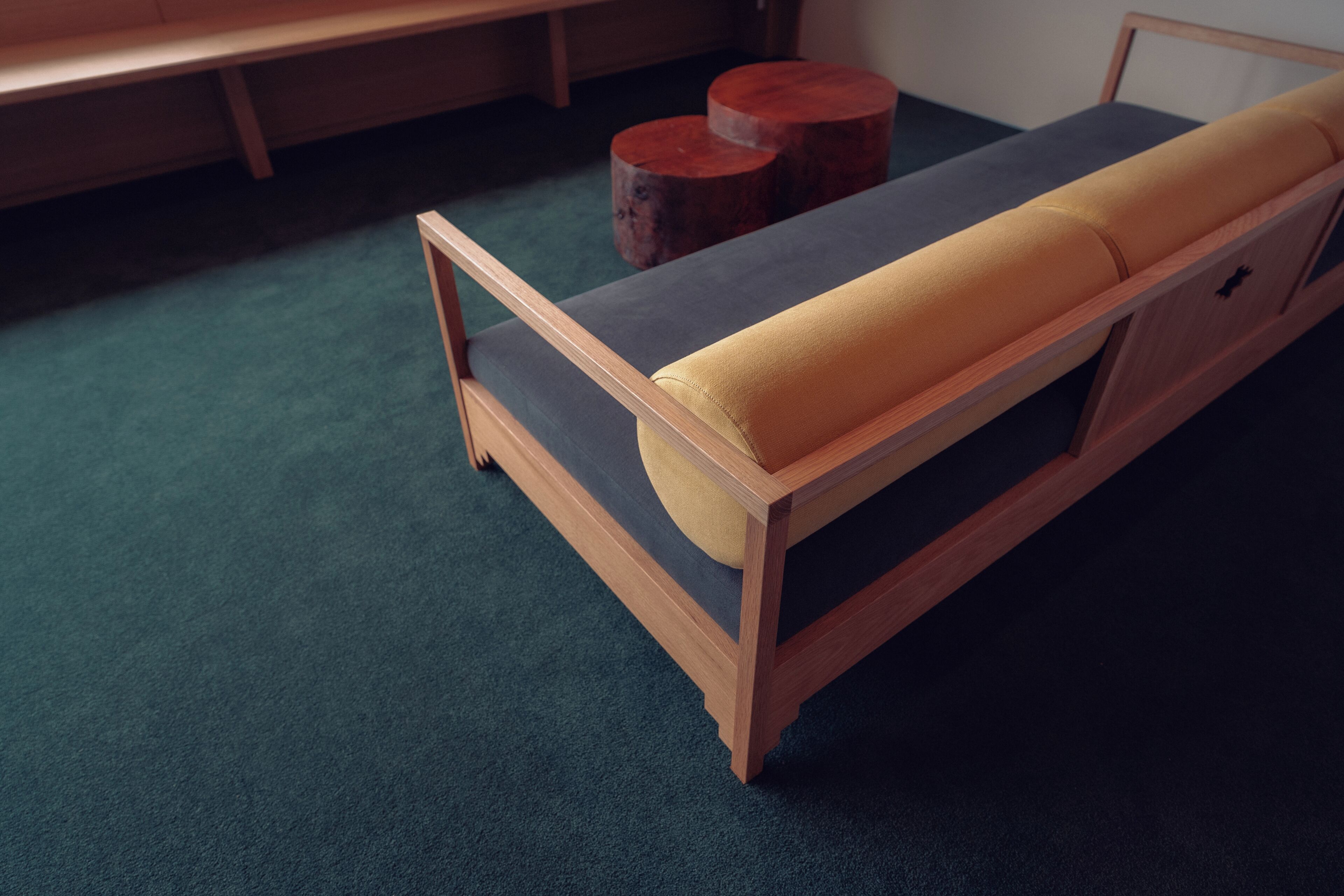Una cama de madera con colchón gris y almohada amarilla en una habitación con alfombra verde.