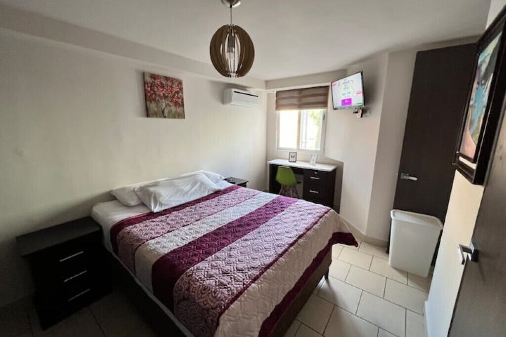 Un dormitorio con cama, escritorio, silla, televisor y ventana.