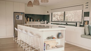 A modern kitchen with a central island, bar stools, a large window, and a seating area with cushions. - The Tides - Luxury Accommodation in Coles Bay (Glamorgan-Spring Bay)