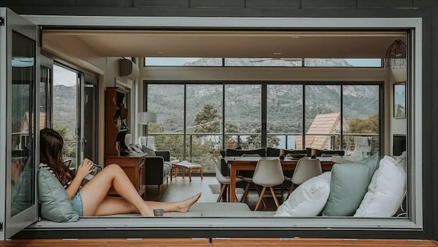 A modern interior with a large sliding glass door leading to a balcony, a seating area with cushions, and a dining table. - The Tides - Luxury Accommodation in Coles Bay (Glamorgan-Spring Bay)