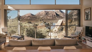 A modern living room with large windows, a ceiling fan, and a view of mountains. - The Tides - Luxury Accommodation in Coles Bay (Glamorgan-Spring Bay)