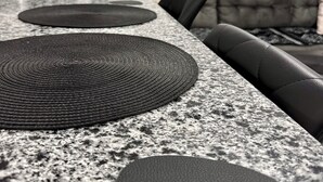 A kitchen with granite countertops, a black woven placemat, and a modern design.