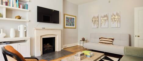 A living room with a fireplace, a sofa, a coffee table, and a bookshelf with books and decorative items.