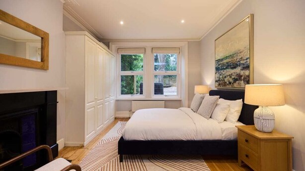 A bedroom with a bed, bedside table, lamp, and a fireplace.
