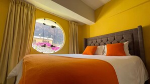 Ein Hotelzimmer mit einem großen Bett, einem runden Fenster mit Blick auf ein Gebäude und Berge, sowie Vorhängen.
