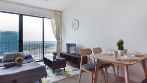 Ein modernes Wohnzimmer mit Sofa, Couchtisch, Esstisch mit Stühlen, Fernseher und Blick auf eine Stadtlandschaft durch große Fenster.