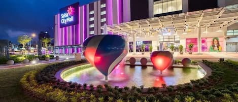 A modern building with a large sign for 'Setia City Mall' and a circular water feature with illuminated spheres.