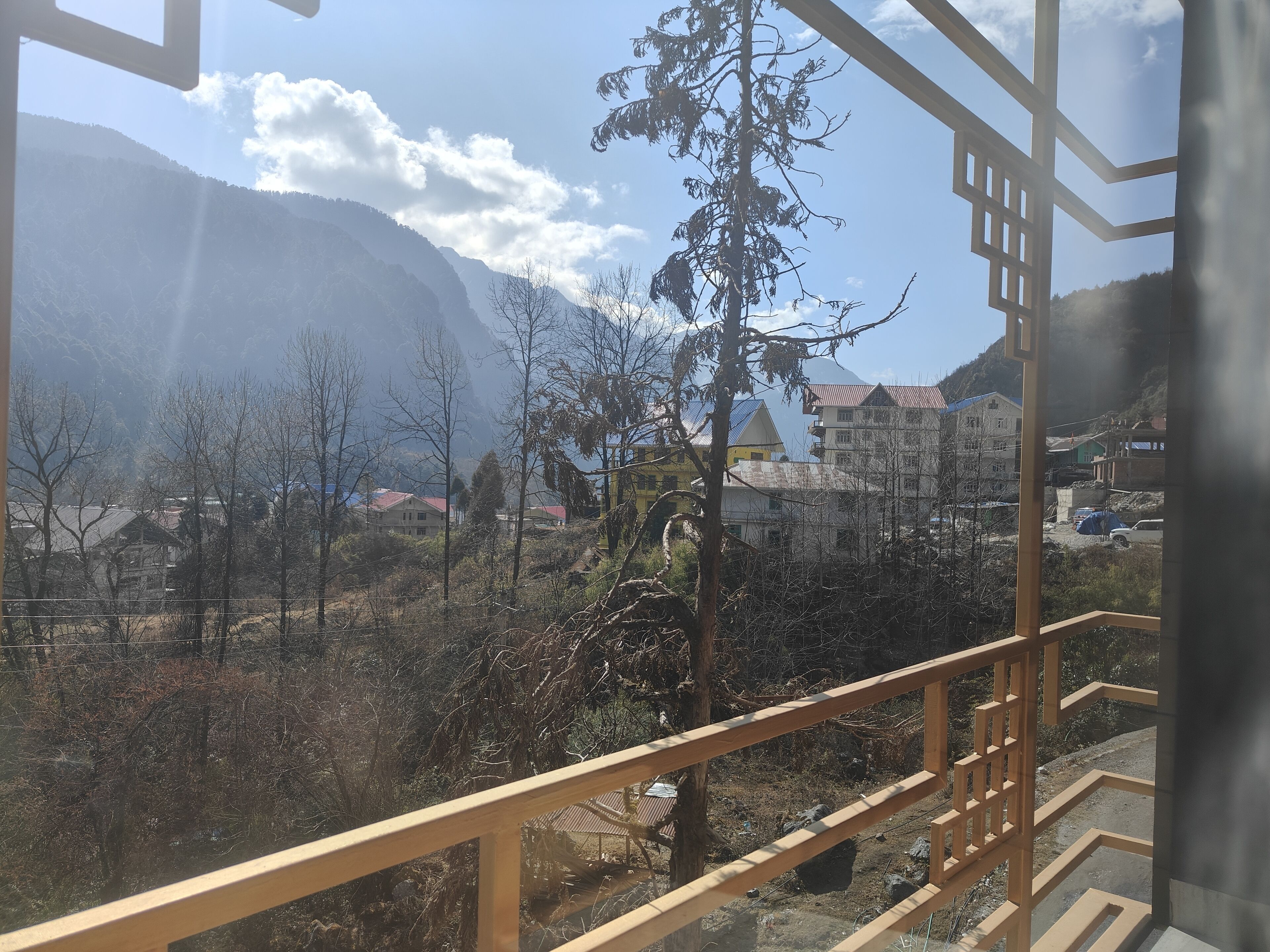 A view from a balcony with a railing, overlooking a mountainous landscape with buildings and trees.