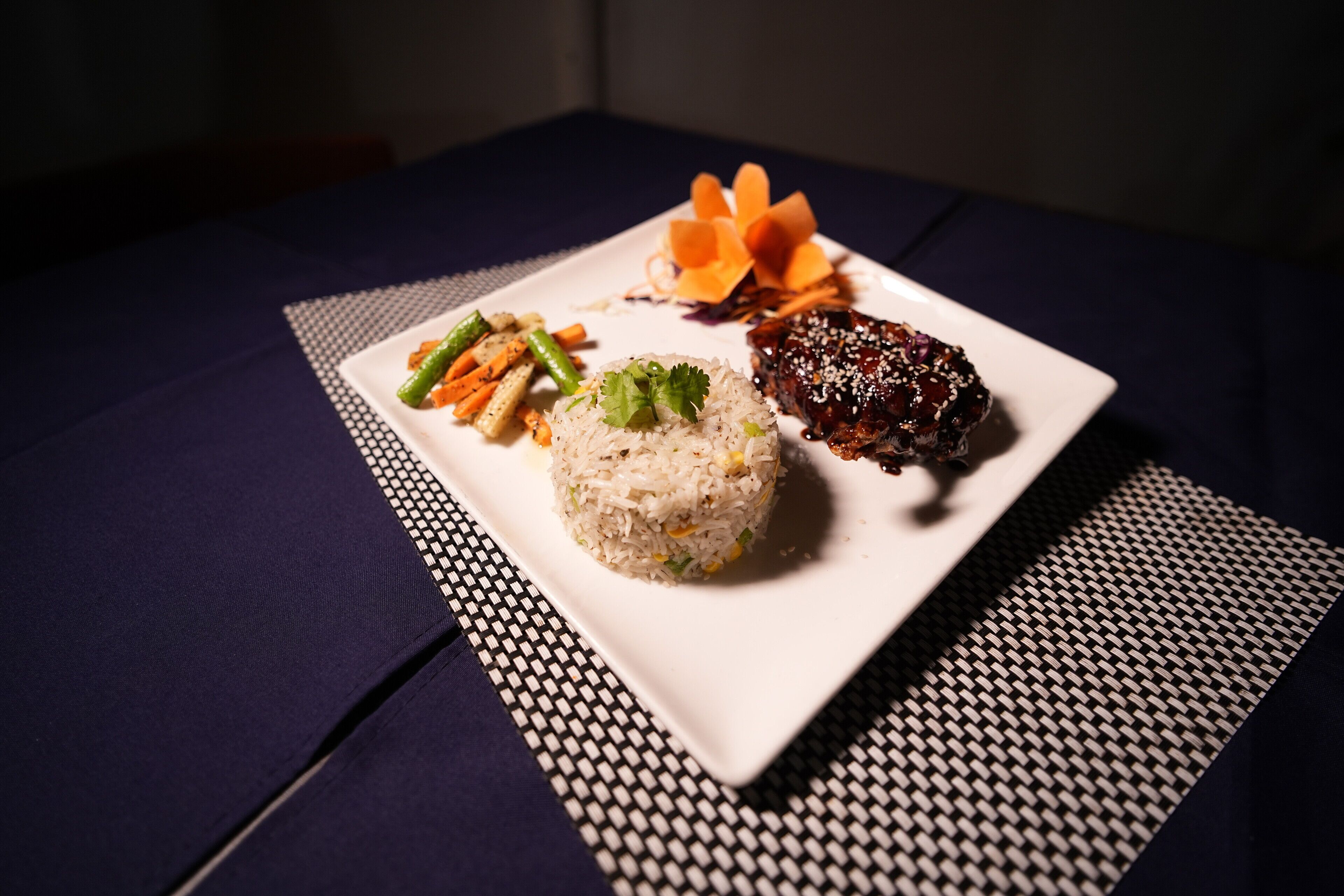 Un plato de comida con arroz, verduras y un guiso de carne, servido sobre un plato blanco con una servilleta de diseño blanco y negro.