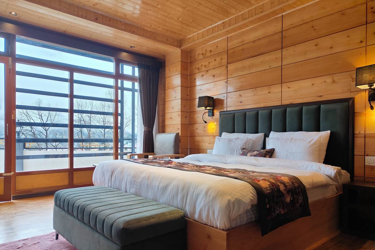 A wooden-paneled bedroom with a large bed, a bench, and a view through a large window.