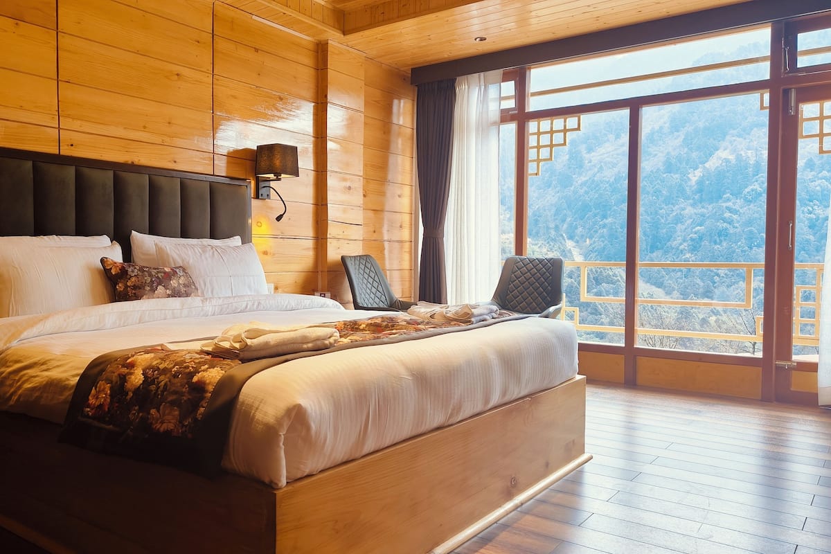 A wooden-paneled bedroom with a large bed, two bedside lamps, and a view of snow-covered mountains through a large window.