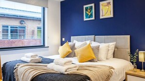 Une chambre à coucher avec un lit, des oreillers, une table de chevet, une lampe et des œuvres d’art accrochées au mur.