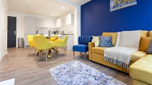 Un salon moderne avec un canapé jaune, un mur bleu et un coin repas avec des chaises jaunes.