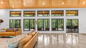 A spacious living area with a high ceiling, large windows, and a polished floor.