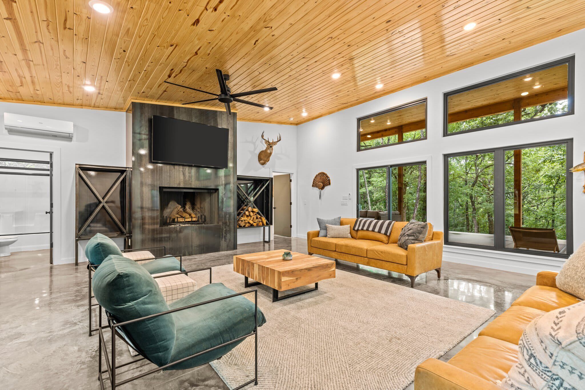 A modern living room with a fireplace, large windows, and a ceiling fan.