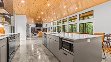 A modern kitchen with a large island, stainless steel appliances, and a wooden ceiling.
