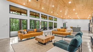 A spacious living area with large windows, wooden ceiling, and modern furniture.