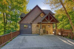 Rustic cabin-style building with a steeply pitched roof and wooden porch, set amidst lush greenery.