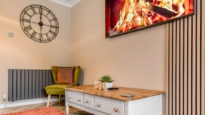 Un salon avec une table basse en bois, un fauteuil vert, une horloge et une cheminée.