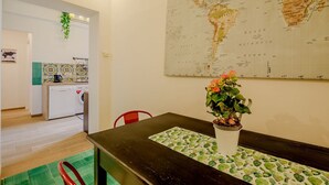 Ein Zimmer mit Esstisch, einem Blumentopf, einer Karte an der Wand und einer Küchenzeile inklusive Waschmaschine.