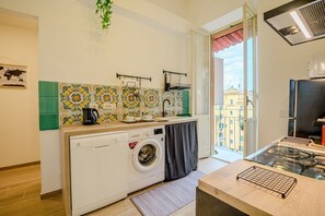 A compact kitchen with a washing machine, a stove, and a view of the city through the window. - Candia Cento Apartment Vatican Museums (Rome)
