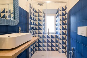 A modern bathroom with a geometric tile pattern, a large sink, and a glass shower enclosure. - Candia Cento Apartment Vatican Museums (Rome)