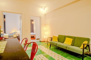 A living room with a green sofa, red chairs, a dining table, and a patterned floor.