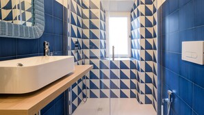 Ein modernes Badezimmer mit geometrischem Fliesenmuster, einem großzügigen Waschbecken und einer Glasdusche.