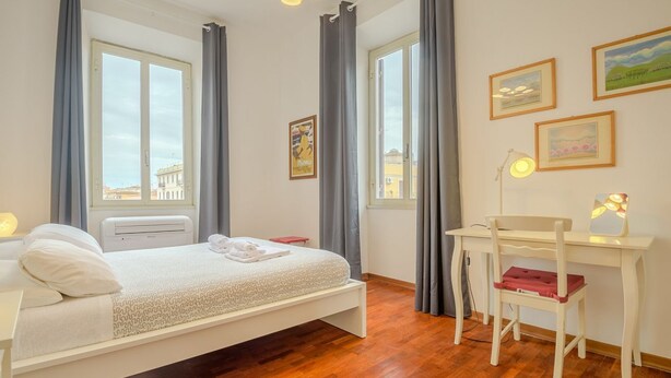 Ein Schlafzimmer mit einem Bett, einem Schreibtisch, einem Sessel und einem Fenster mit Vorhängen.
