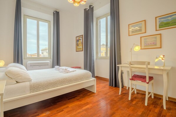 A bedroom with a bed, a desk, a chair, and a window with curtains.