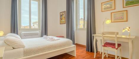 Ein Schlafzimmer mit einem Bett, einem Schreibtisch, einem Sessel und einem Fenster mit Vorhängen.