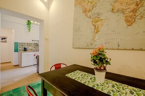 A room with a dining table, a potted plant, a map on the wall, and a kitchen area with a washing machine. - Candia Cento Apartment Vatican Museums (Rome)