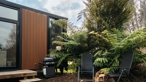 A modern outdoor patio with a wooden table and chairs, a barbecue grill, and a fire pit. - Kiwi Farm Cabin 2 by Tiny Away (Waitoki)