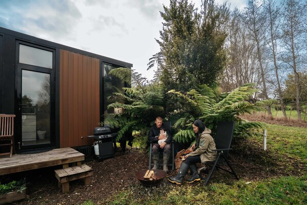 A modern house with a deck, a barbecue area, and a large tree in the backyard.