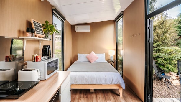 A compact bedroom with a bed, bedside table, and a view of the outdoors. - Kiwi Farm Cabin 2 by Tiny Away (Waitoki)