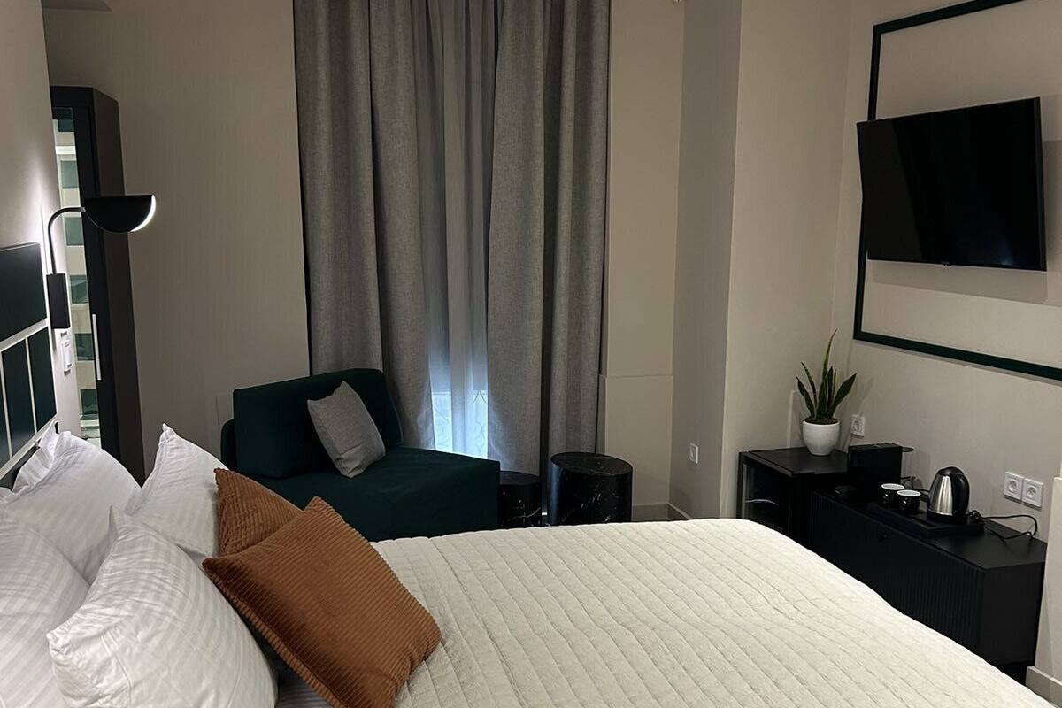 A modern hotel room with a large bed, a flat-screen TV mounted on the wall, a small side table, and a window with curtains.