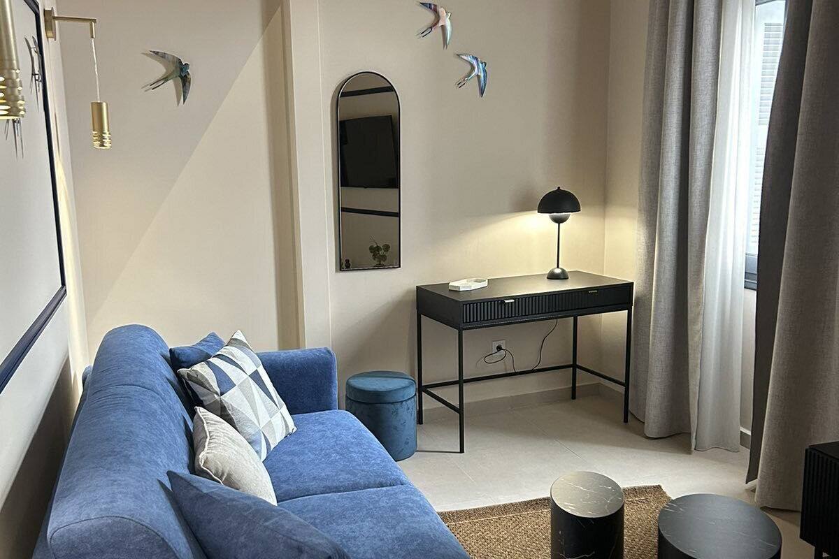 A modern living room with a blue sofa, a small desk, a mirror, and decorative bird wall art.