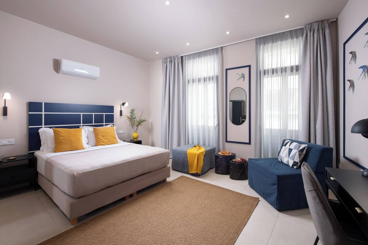A modern hotel room with a large bed, a sofa, a desk, and a mirror.