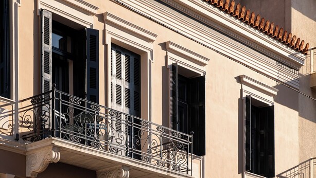 A building with a balcony, large windows, and a door with a decorative grille. - Living Yard Thissio (Athens)